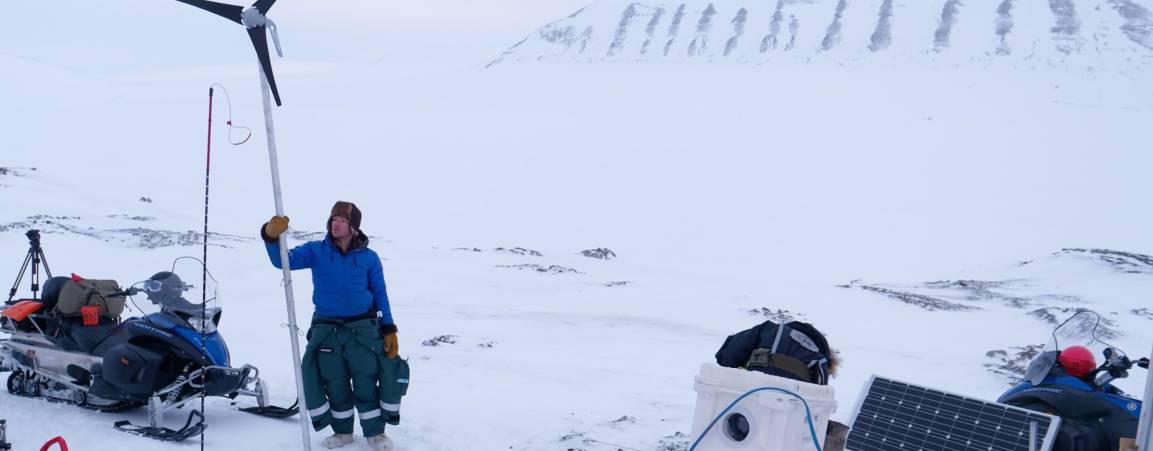 Two researchers looking out towards the tundra while another researcher is setting up equipment